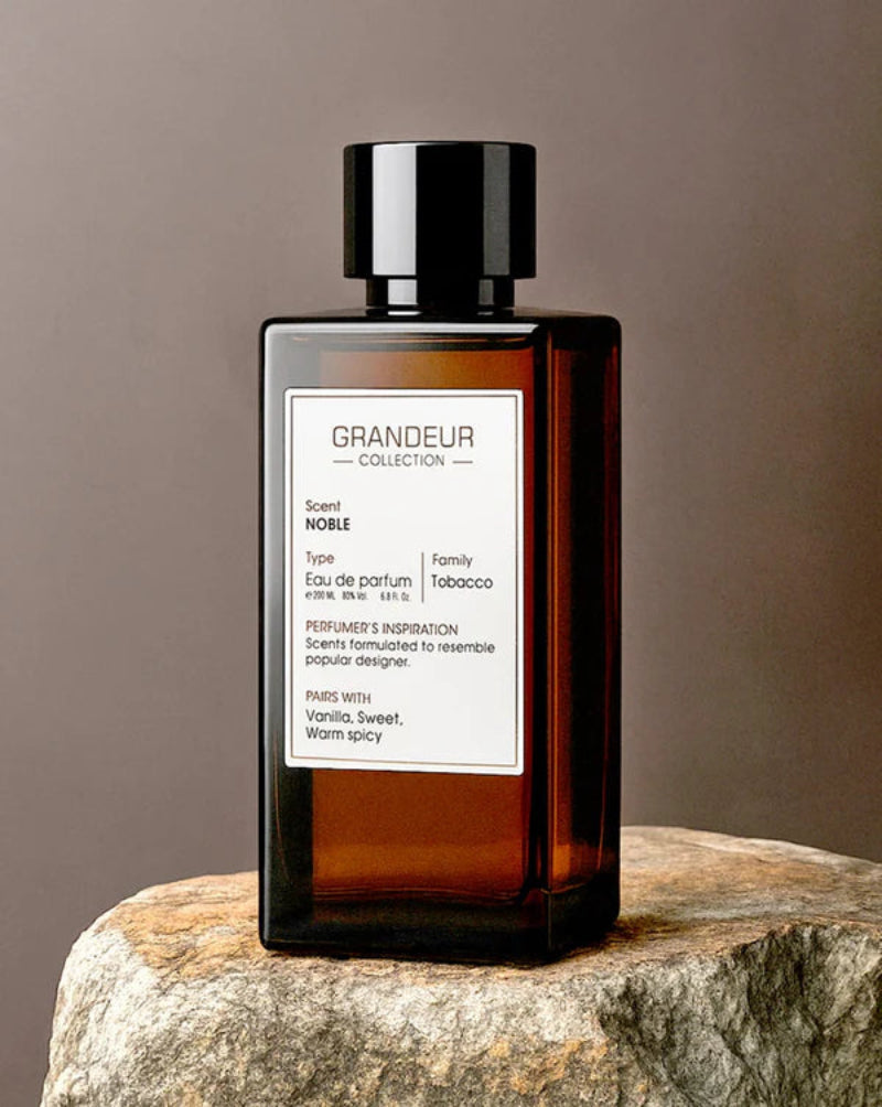 Perfume bottle labeled 'Grandeur Collection' on a stone surface with a neutral background