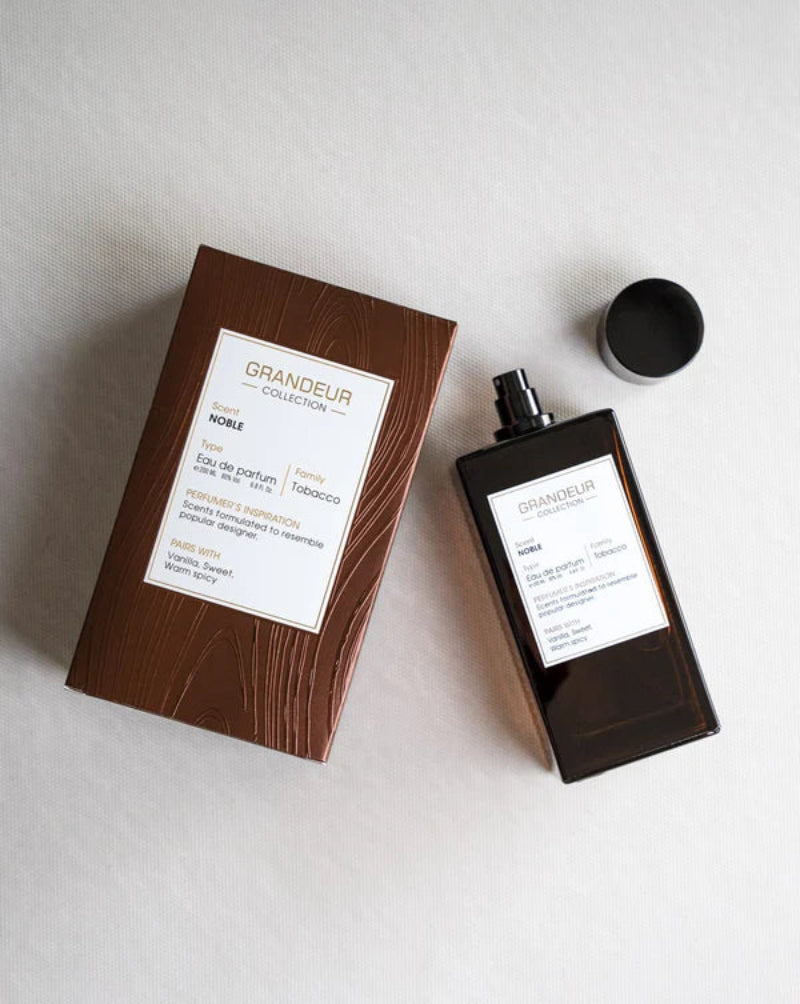Perfume bottle and packaging with 'Grandeur' branding on a light background