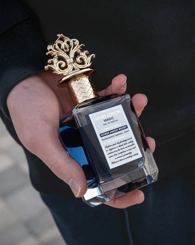 Hand holding a decorative perfume bottle with a gold cap against a dark background