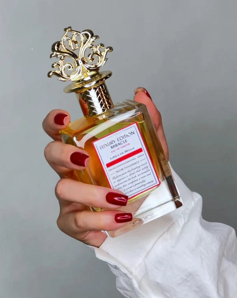 Hand holding a perfume bottle with a decorative gold cap against a gray background