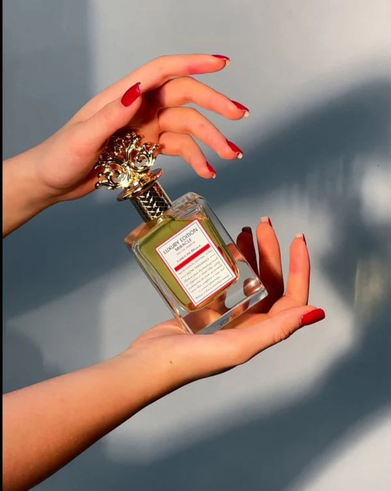 Hand holding a perfume bottle with a decorative cap against a neutral background